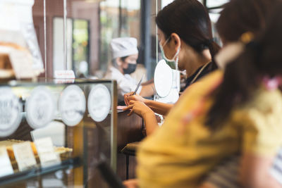 Woman customer in protective mask signing on receipt at counter in cafe