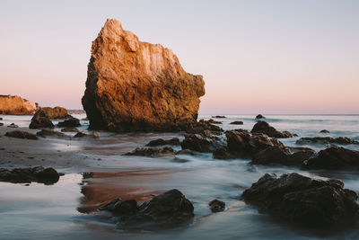 Rocks on beach against sky during sunset