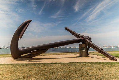 Large metal anchor at beach against blue sky