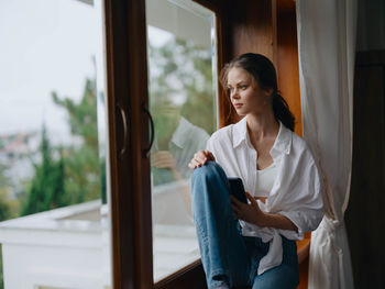 Side view of young woman looking through window