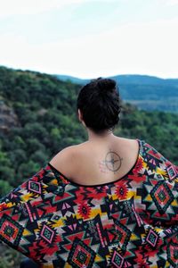 Rear view of young woman with tattoo on back standing against sky