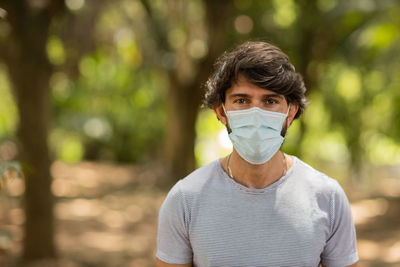 Handsome man wearing a medical protective mask on his face on a sunny day at park.