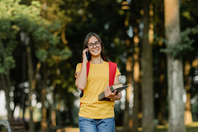 Portrait of a beautiful brunette with glasses and a backpack talking on the phone in the park