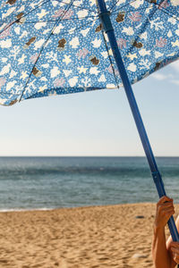 Cropped hand holding blue parasol at beach on sunny day