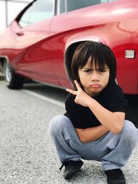 Portrait of boy gesturing while crouching by car parked on footpath