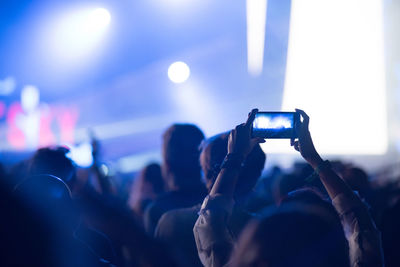 Cropped hands of woman filming over smart phone at music concert