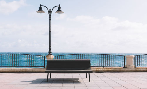 Empty bench at promenade against sky