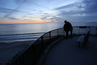 Rear view of silhouette man standing at beach during sunset