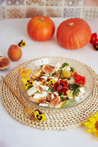 Fresh autumn vegetarian salad with edible flowers, figs, peach, greens and feta on ceramic tile 