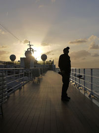 Rear view of silhouette man standing by railing against sky