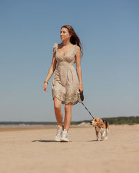 Side view of young woman with dog on beach against clear sky