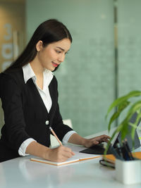 Smiling businesswoman writing on diary at office