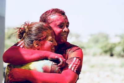 Close-up of couple covered with powder paint embracing against sky