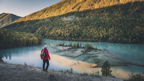 Rear view of woman standing by lake against sky