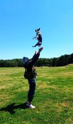 Side view of man throwing dog against clear blue sky