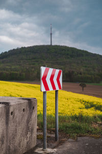Sign board on field against sky