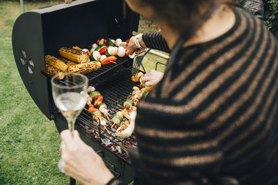 Midsection of woman holding drink while barbecuing dinner at back yard