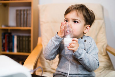 Cute boy looking away while inhaling through respiratory mask at home