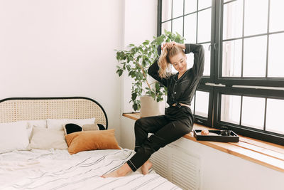 Woman sitting on bed by window at home