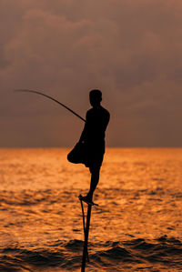 Silhouette man fishing in sea against sunset sky