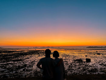 Rear view of woman standing at beach against sky during sunset