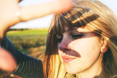 Close-up of young woman shielding eyes while standing at field against sky on sunny day