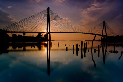 Silhouette barelang bridge over river against cloudy sky during sunset