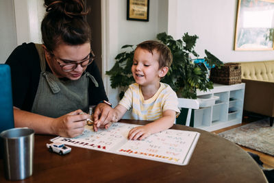 Mom painting smiling son's finger nails at kitchen table