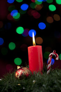 Close-up of lit candle with christmas decorations against illuminated lights