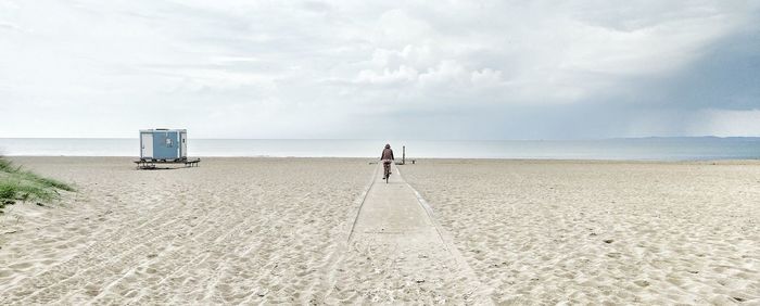 Rear view of person cycling at sandy beach against sky