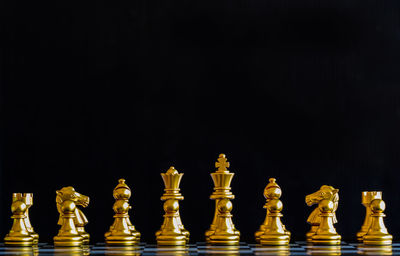 Close-up of golden chess pieces on board against black background