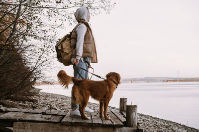 Young woman and dog retriever walks on river shore at autumn season