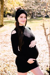 Portrait of smiling pregnant woman standing against tree