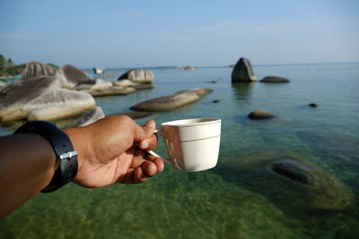 Midsection of man holding ice cream in sea against sky