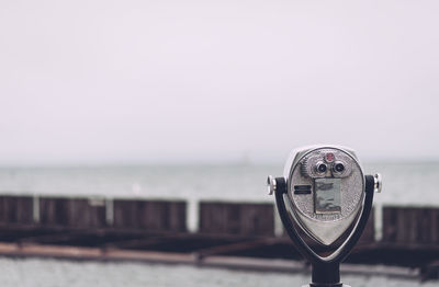 Close-up of coin-operated binoculars by sea against clear sky