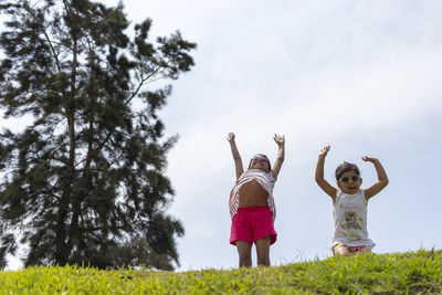 Low angle view of sisters playing on grass against sky