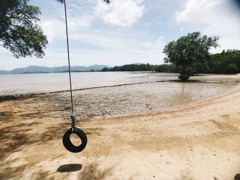 Empty swing hanging on beach against sky