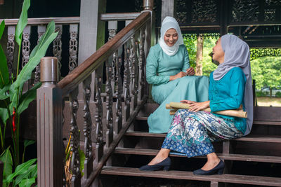 Full length of a smiling young woman sitting on railing