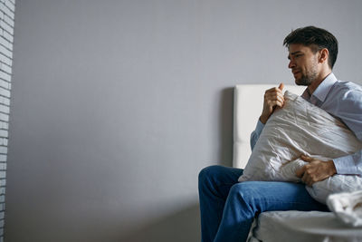 Man sitting on sofa against wall at home