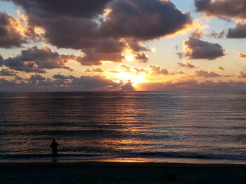 Silhouette woman standing on beach against sky during sunset