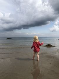 Rear view of girl standing on beach against sky