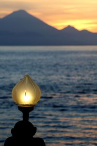 Illuminated lamp by sea against sky during sunset