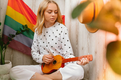 Young millennial hippie woman sitting on balcony play guitar. music lesson and singer sitting. lgbtq 