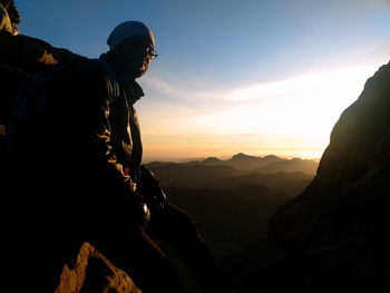 Man leaning on rock against sky during sunset