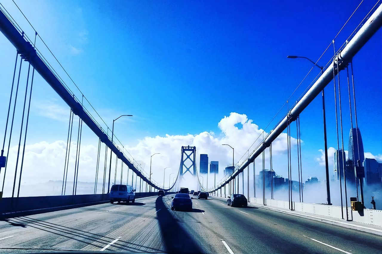 transportation, architecture, sky, built structure, city, bridge, road, suspension bridge, motor vehicle, car, cable-stayed bridge, nature, mode of transportation, street, travel, blue, travel destinations, cloud, building exterior, the way forward, city life, traffic, cityscape, no people, sign, land vehicle, day, highway, sunlight, line, outdoors, motion, street light, symbol, tourism, cable, urban skyline, clear sky, building, steel cable, on the move, city street, overpass, diminishing perspective, sunny