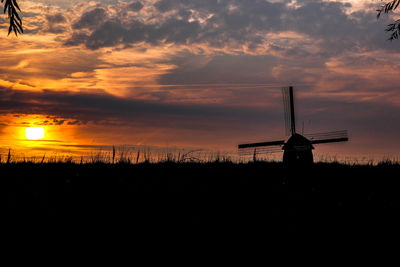 Silhouette of traditional windmill in a field at sunset