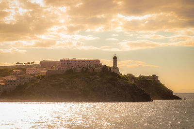 Buildings by sea against sky during sunset