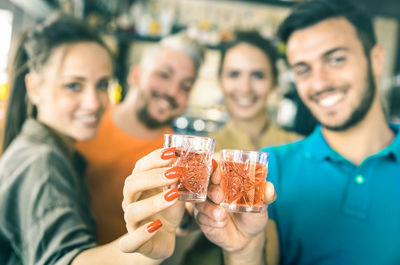 Portrait of happy friends holding drinks while standing in bar