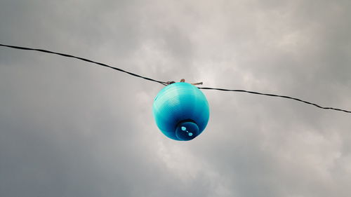 Low angle view of lantern hanging on cable against cloudy sky