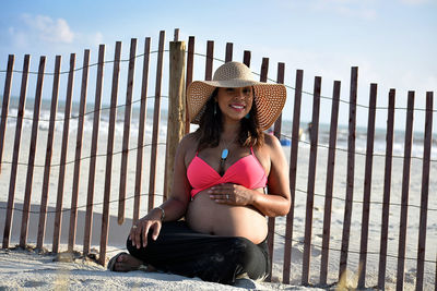 Young woman wearing hat sitting against sky